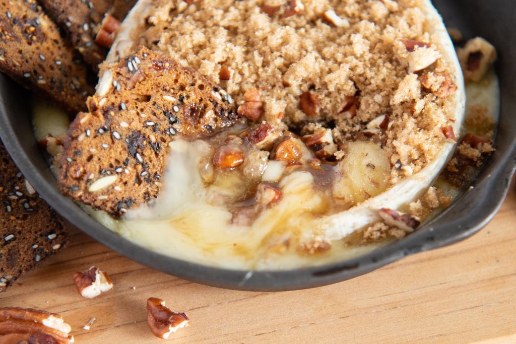 a cracker stuck into a wheel of baked brie with brown sugar and pecans on top it