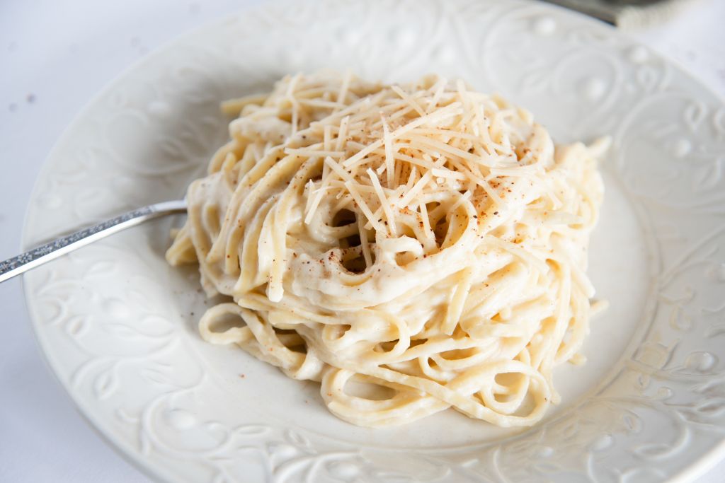 noodles with sauce and cheese on them on a white plate, there is a fork next to them too