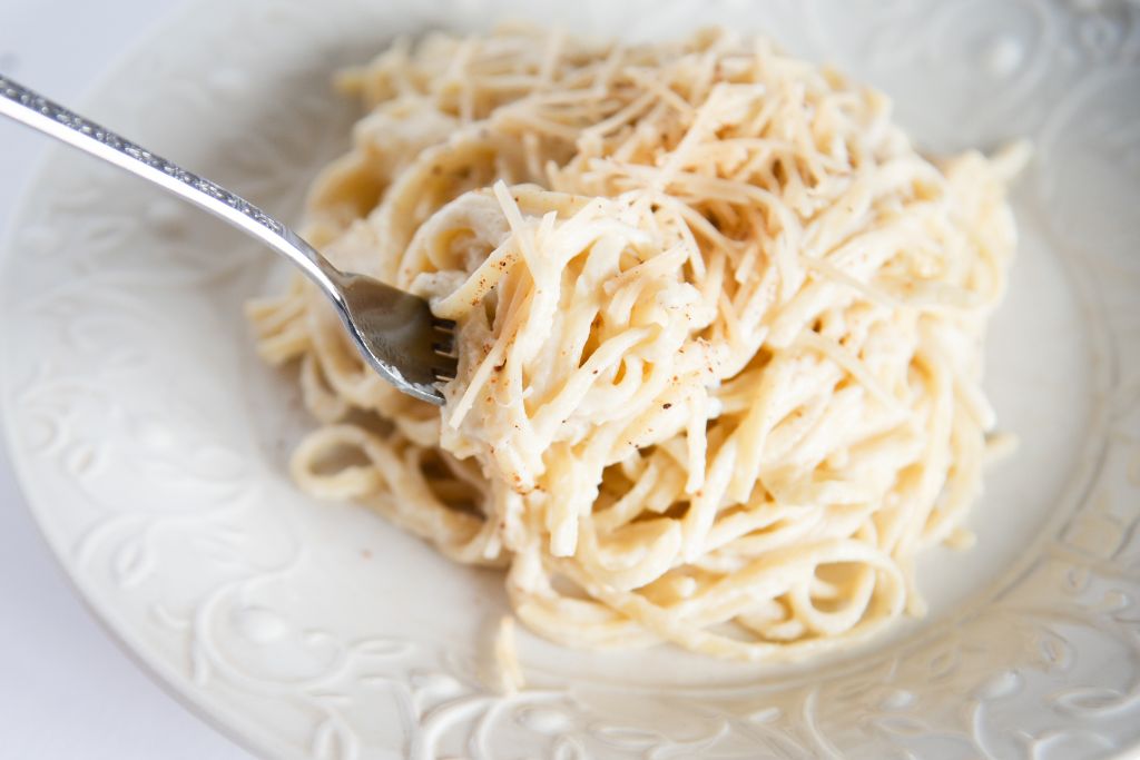 a fork full of sauce covered noddles being held in front of a plate of noodles