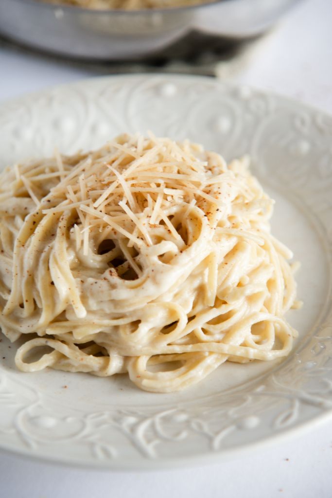 noodles covered in cauliflower Alfredo sauce on a white plate, there is cheese and nutmeg sprinkled on top of them