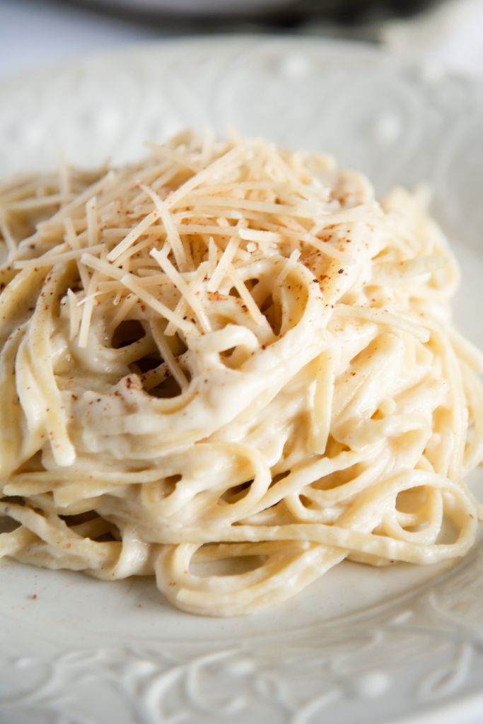 a close up of cauliflower alfredo sauce covered noodles on a white plate