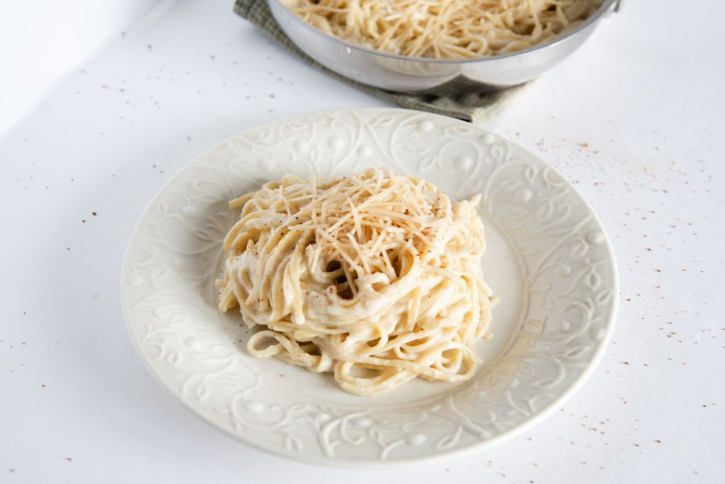 a plate of sauce covered noodles with cheese and nutmeg on top, you can see part of a pan of noodles behind the plate