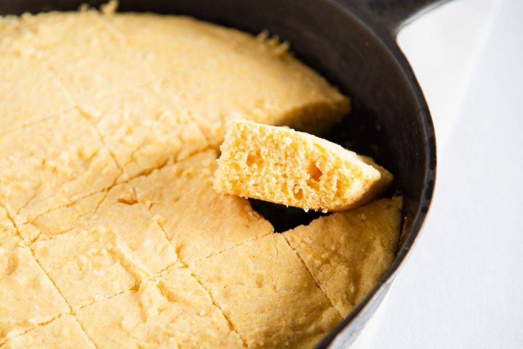 cut cornbread in a cast iron skillet, one piece is tilted upward 