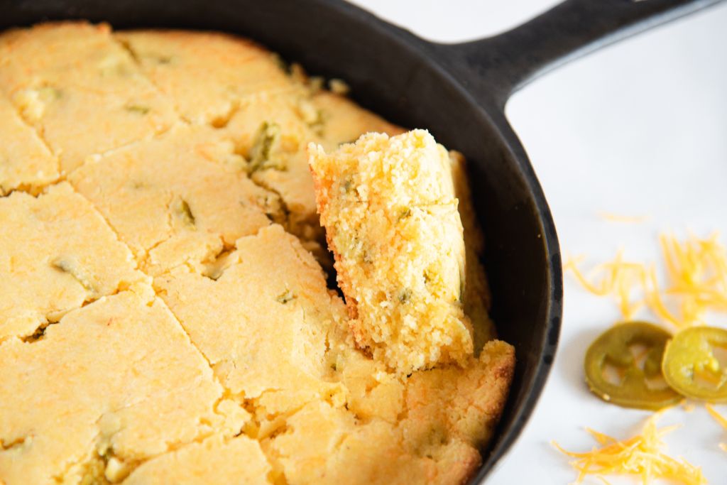 sliced jalapeno cheddar cornbread in a cast iron skillet, one of the piece is tilted upward 