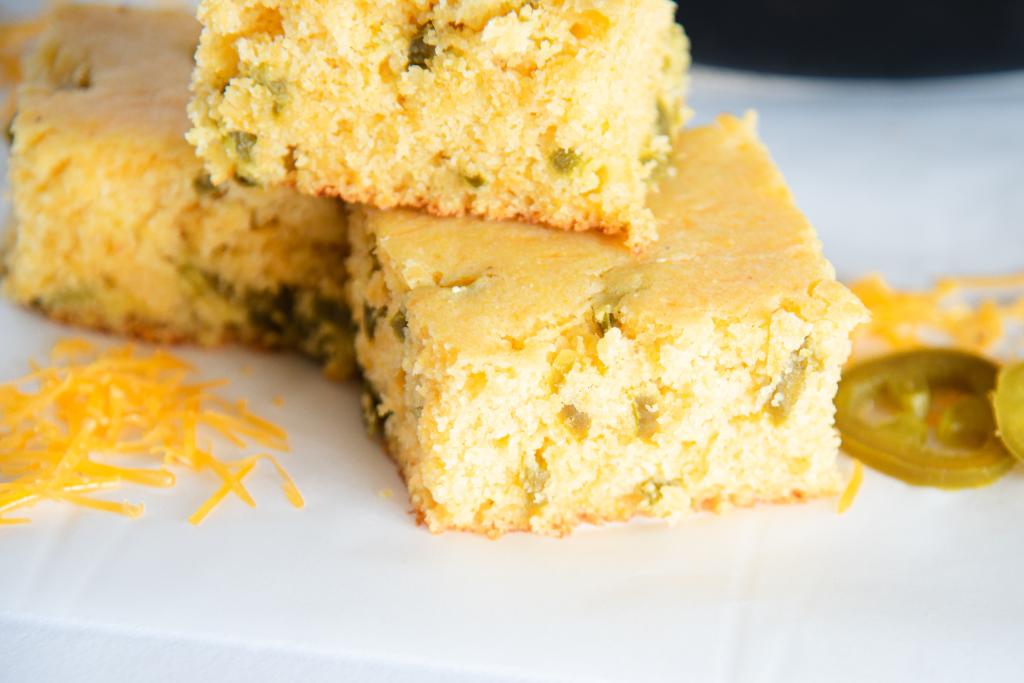 a close up of a stack of jalapeno cheddar cornbread, there is some shredded cheese and some sliced jalapenos next to it