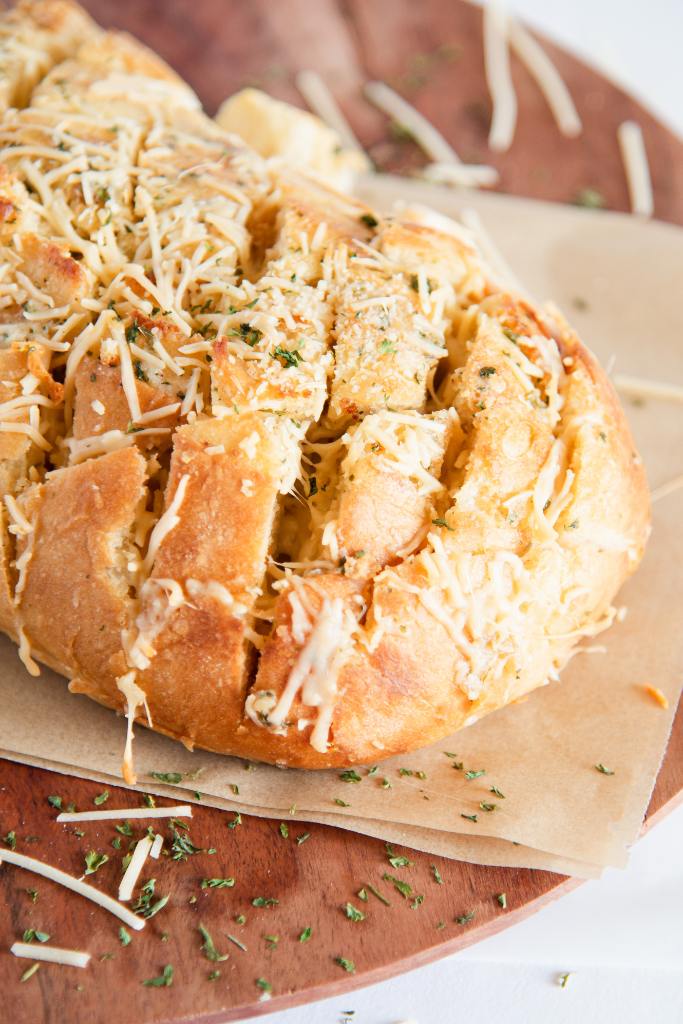 a close up of a loaf of cheesy bread on a wooden cutting board