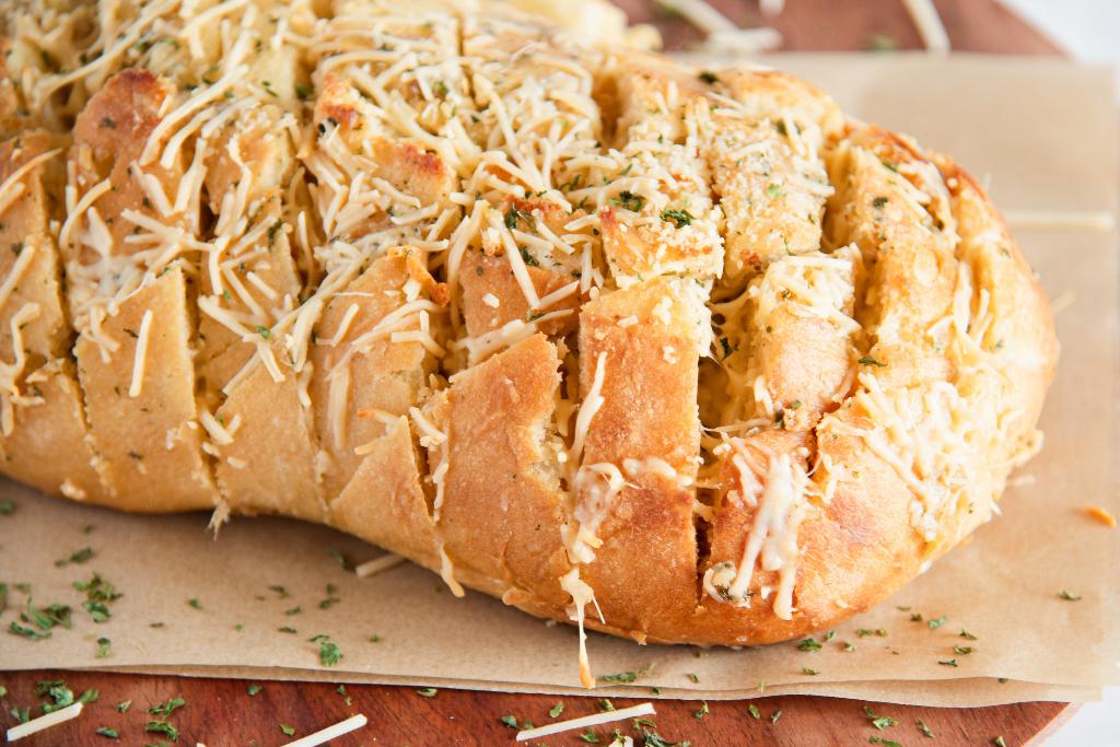 a close up of finished cheesy bread on a wooden cutting board 