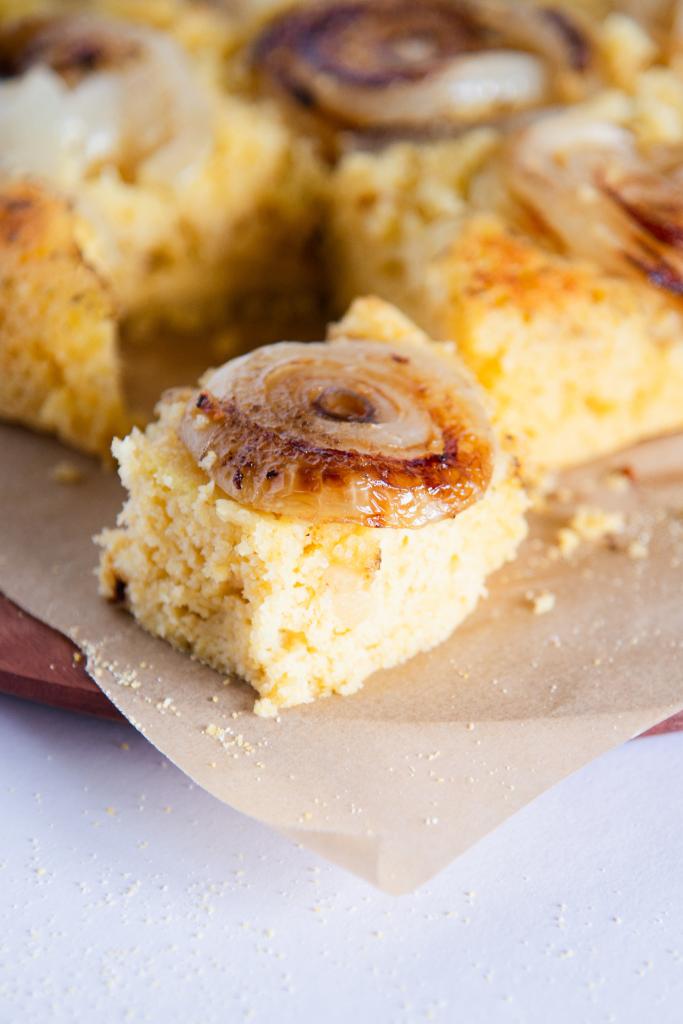 a piece of cornbread with onion on top, you can see the rest of the cut cornbread behind it