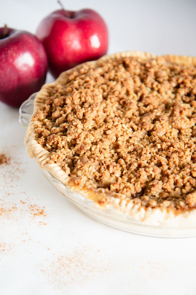 an uncut apple pie with two whole apples behind it