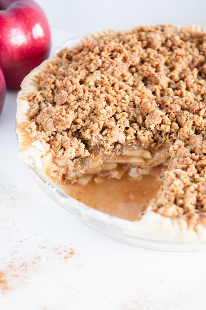 an apple pie with a slice taken out of it. There are also two whole apples to the side of it