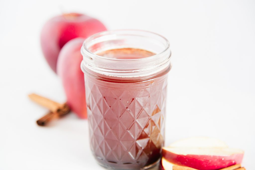 an overhead shot of a jar of apple syrup, there are apple slices and cinnamon stick next it, there are a couple whole apples next to it 