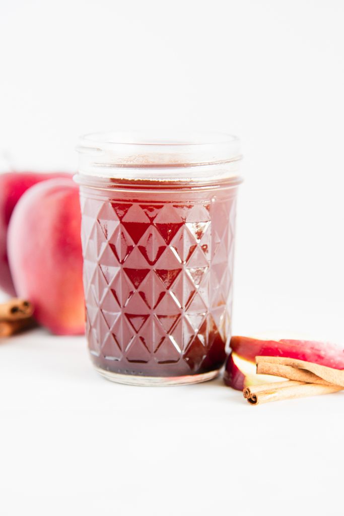 a jar of apple syrup with apple slices and cinnamon sticks next to it