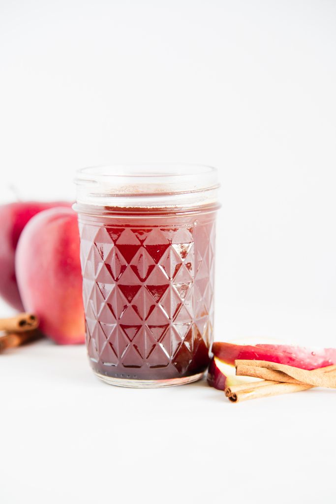 a jar of apple simple syrup with apple slices and cinnamon sticks next to it.