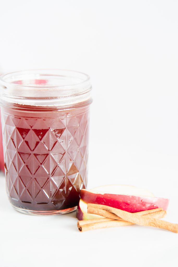 a close up of a jar of apple syrup with apple slices and cinnamon sticks next to it 