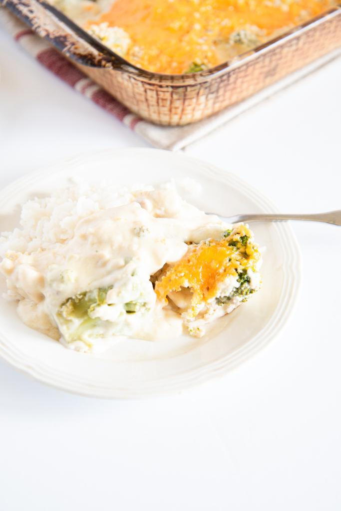 a plate of chicken divan over rice with a fork on it, you can also see part of the pan of divan behind the plate