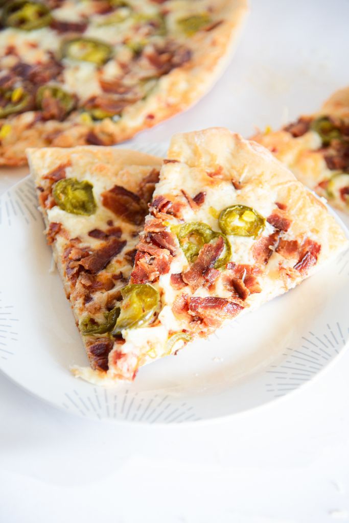 two slices on pizza on a plate, you can see part of the rest of the pizza next to it