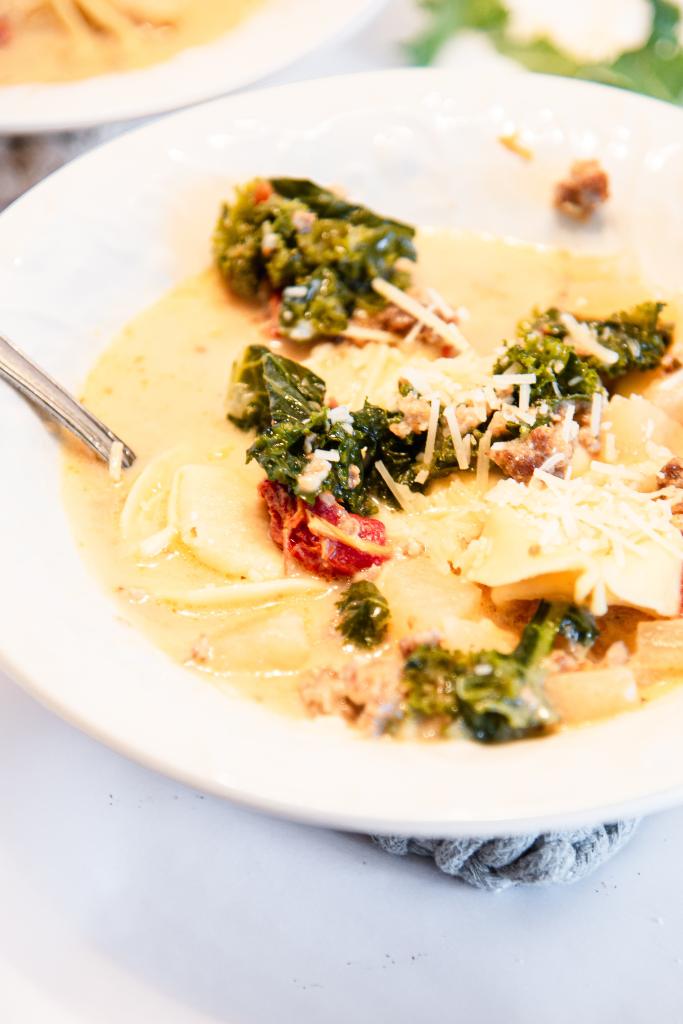 a close up of a bowl of soup with a spoon in it and some shredded cheese sprinkled on top