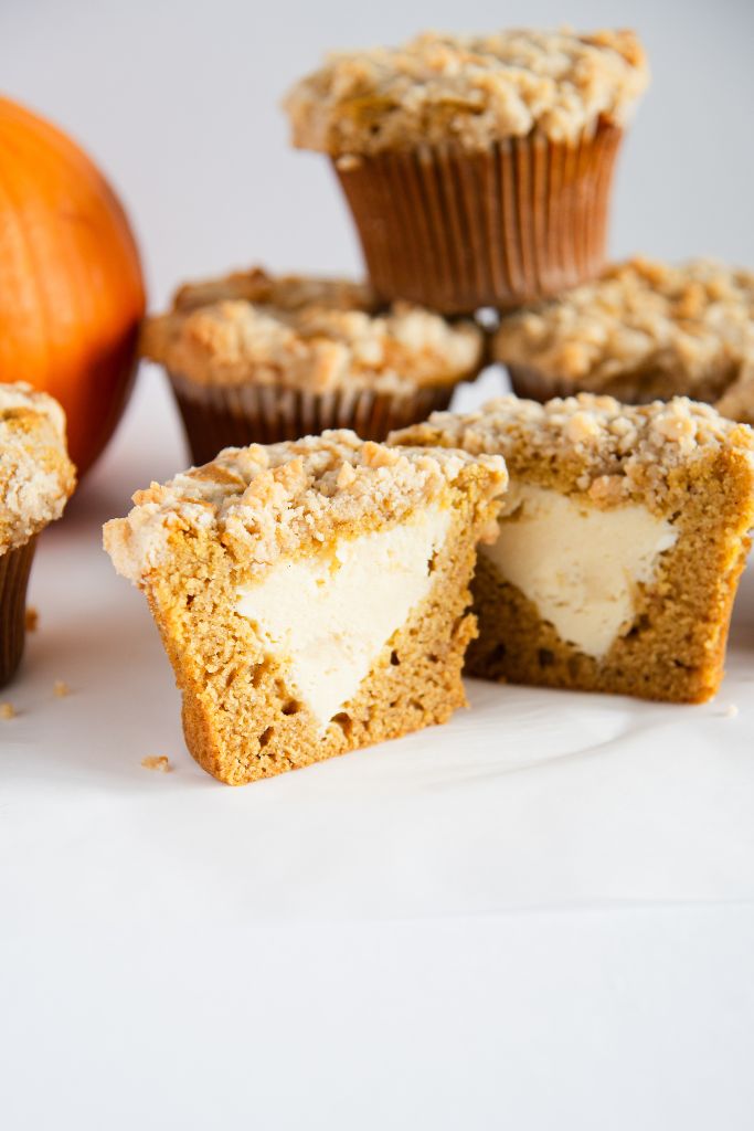 a pumpkin cheesecake muffin that has been cut in half, to show the filling, there some muffins stacked up behind it