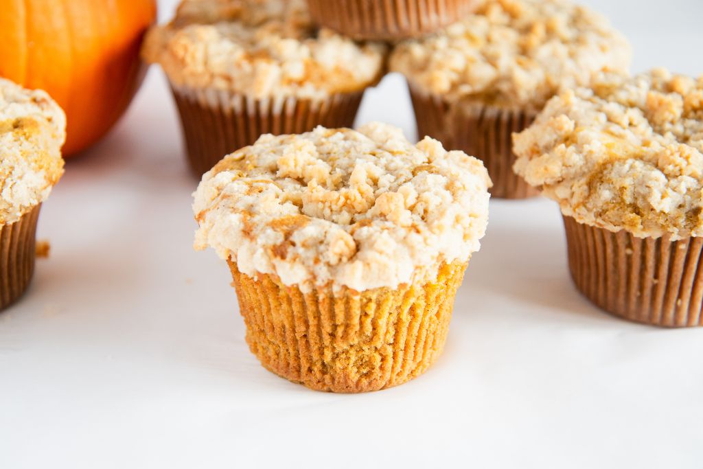 an overhead shot of a pumpkin muffin, there more muffins around it, and you can see part of a pumpkin behind it