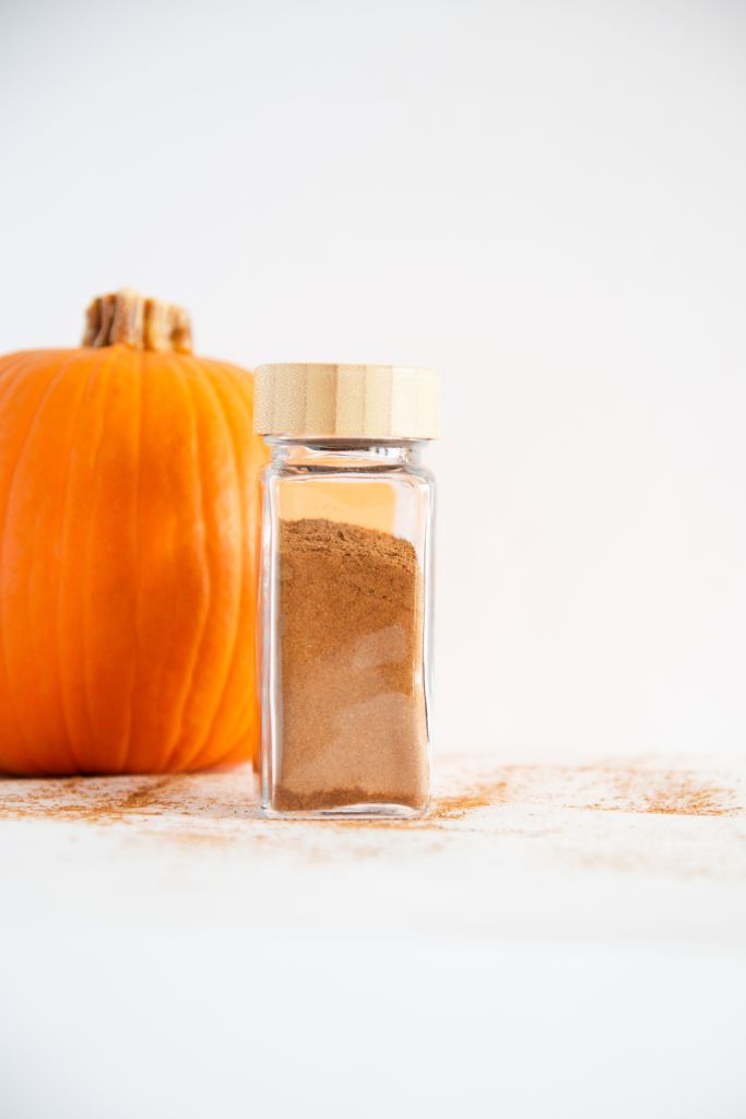 a glass spice bottle of pumpkin pie spice with a pumpkin behind it