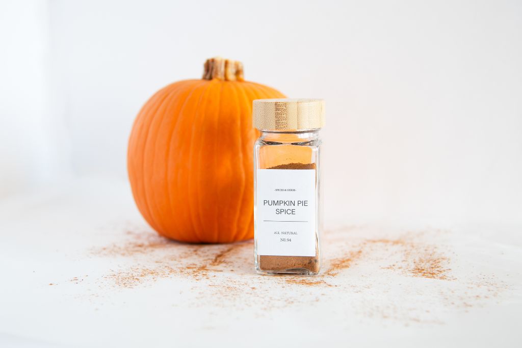 a bottle pf pumpkin pie spice, with a pumpkin behind it