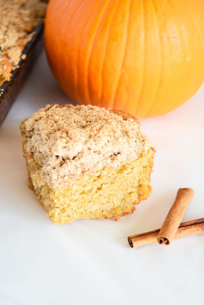 a piece of coffee cake with cinnamon sticks next to it and a pumpkin behind it