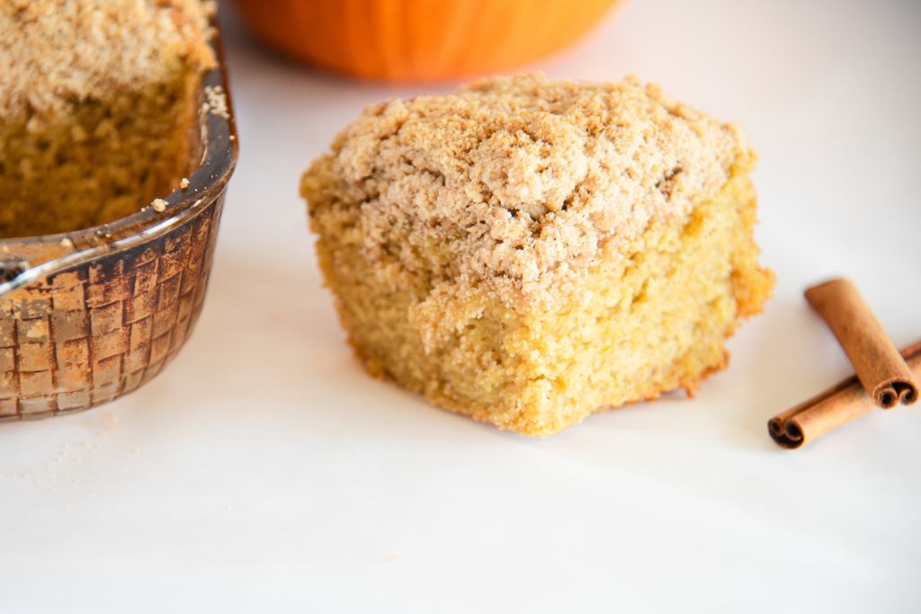 a close up of a piece of coffee cake with cinnamon sticks next to it, there is a pan of coffee cake to the left of it as well