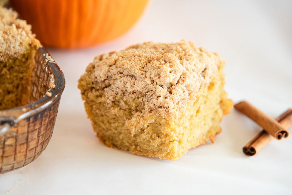 a close up of a piece of coffee cake, there is cinnamon sticks to one side of the piece and pan of coffee cake to the other side