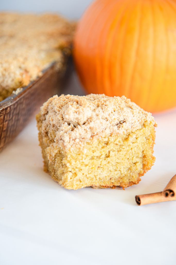 a piece of coffee cake, there is a pan and a pumpkin behind the piece