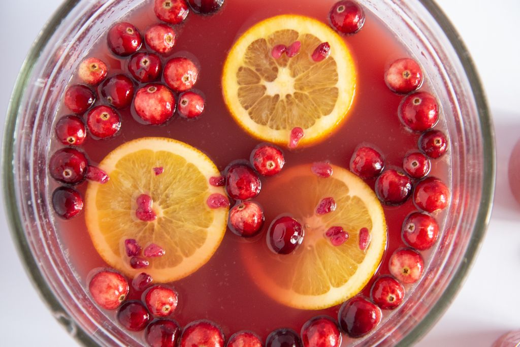 an overhead stop of a bowl of punch with orange slices and cranberries floating in it 