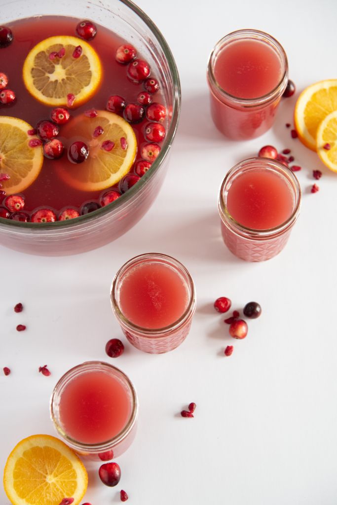 a bowl of punch with 4 cups of punch, and some cranberries and orange slices around them 