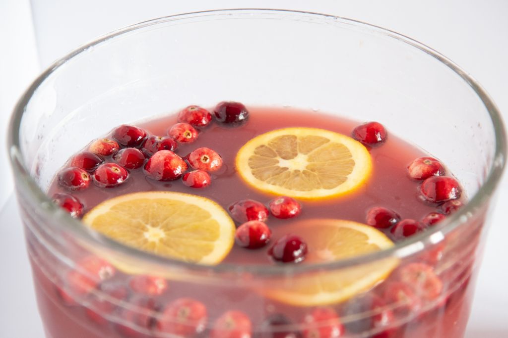 a close up of a bowl of punch with cranberries and orange slices floating in it 