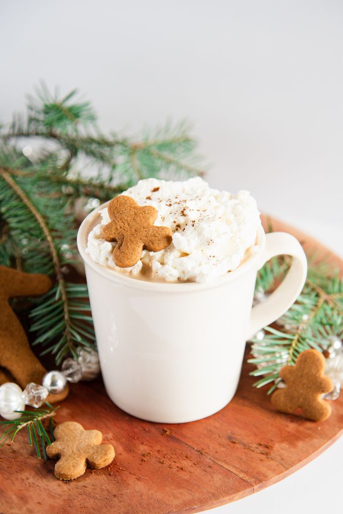 a gingerbread latte with pine branches and little gingerbread cookies around it 