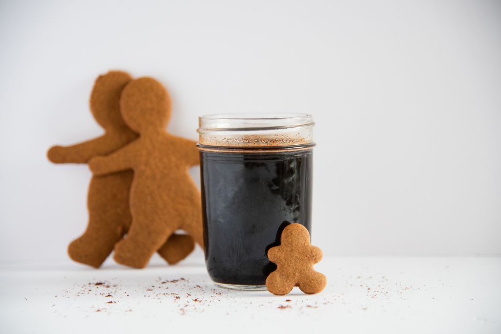 a jar gingerbread syrup with a gingerbread man lined against it, there are also two gingerbread cookies behind it