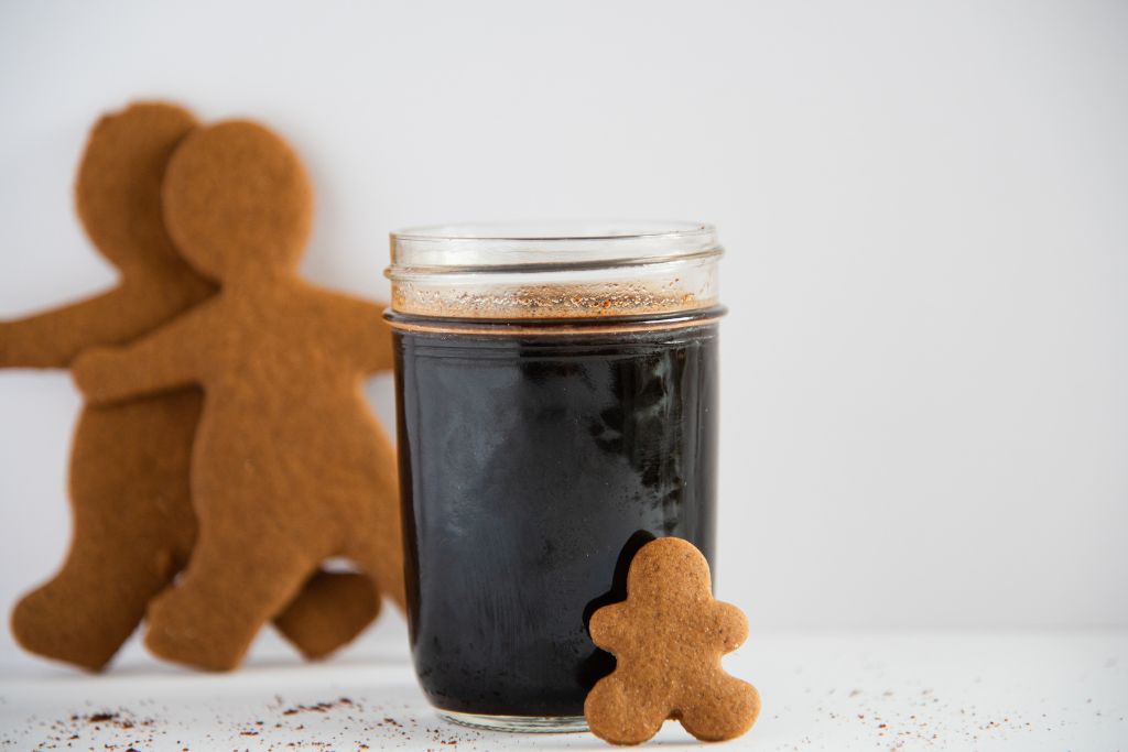 a jar of gingerbread syrup, there is a gingerbread man lining against the jar, and two gingerbread cookies behind it