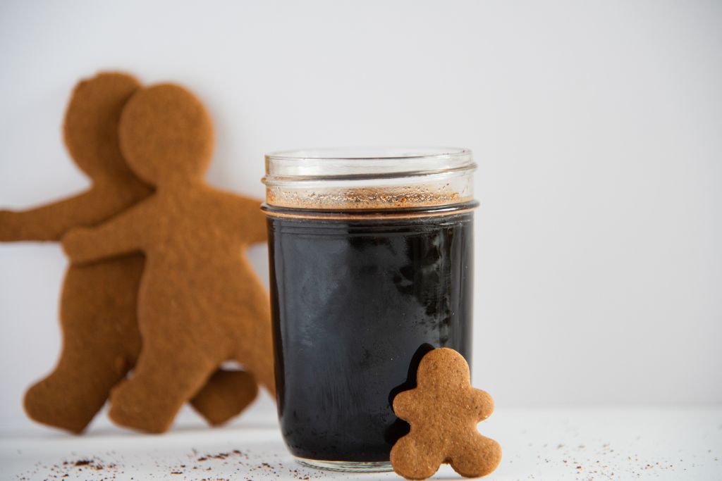 a jar of gingerbread syrup, with a gingerbread man lining against it, there are also two gingerbread cookies behind it