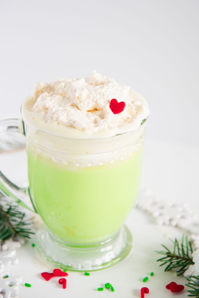 a cup of grinch hot chocolate with just whipped and a single heart sprinkle on top