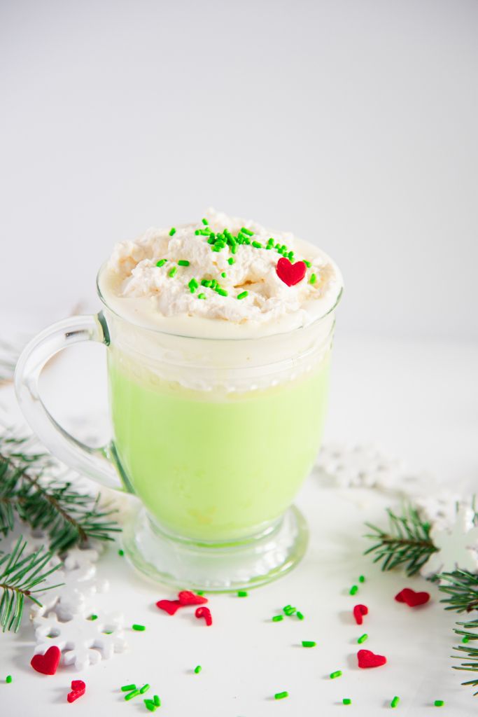 a cup of Grinch hot with pine branches, snowflakes and sprinkles around it