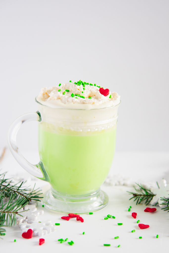 a cup of Grinch hot chocolate with sprinkles around it 