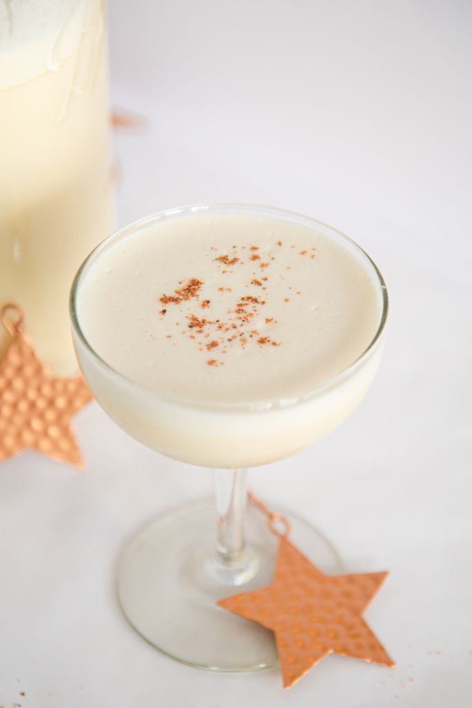 a close up of a glass of eggnog with nutmeg sprinkled on top, there is a gold star next to the glass as well