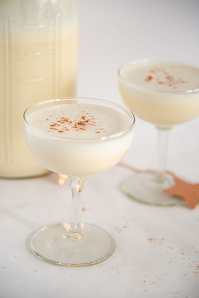 a glass of eggnog, with a second glass behind it, and a jar of eggnog to the side of it.