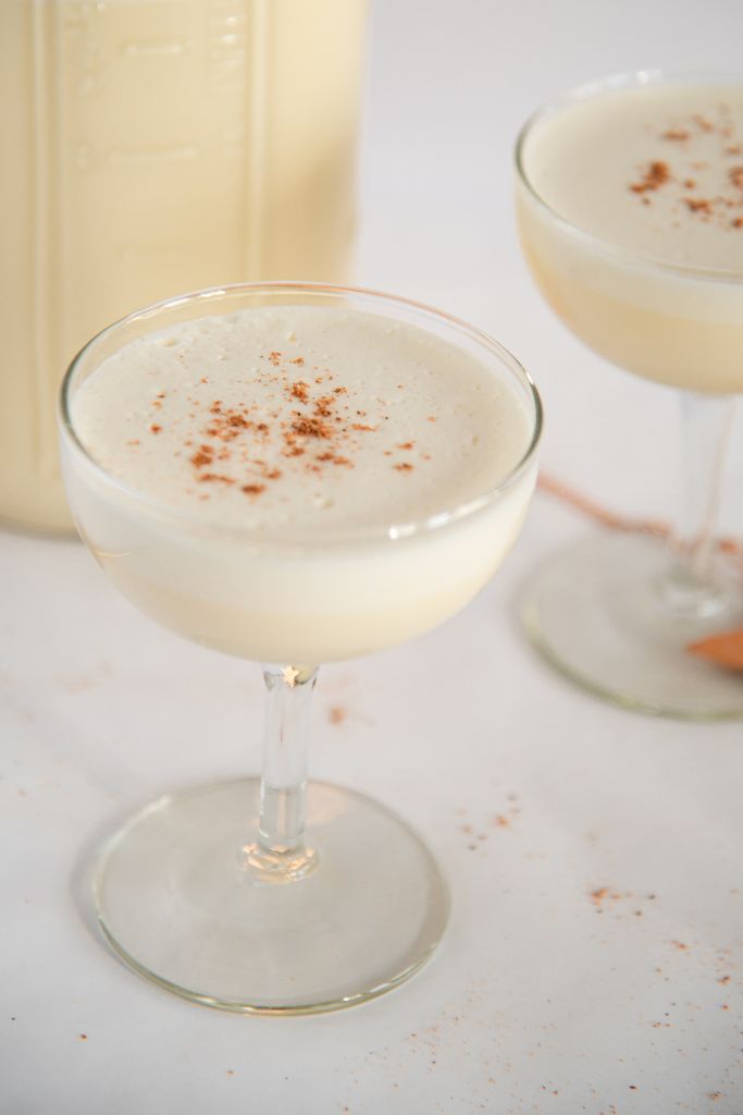 two glass of eggnog with ground nutmeg on top, there is a jar of eggnog and a couple gold stars next to them