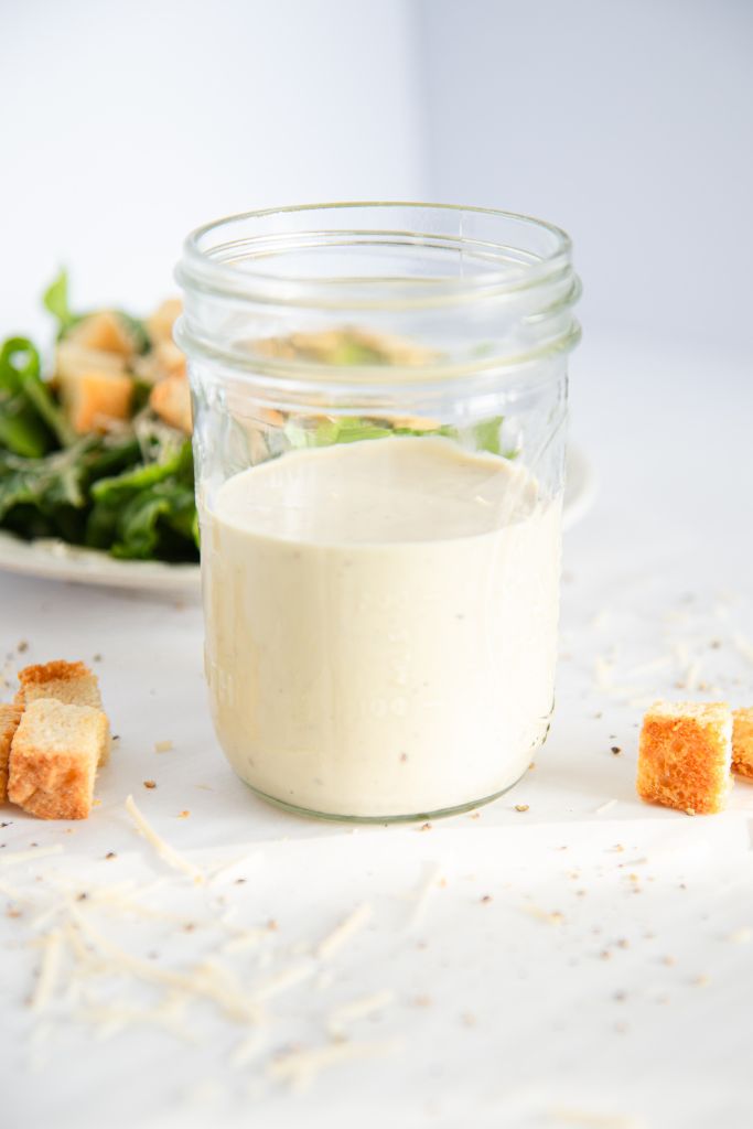 a jar of salad dressing with a plate of salad behind it