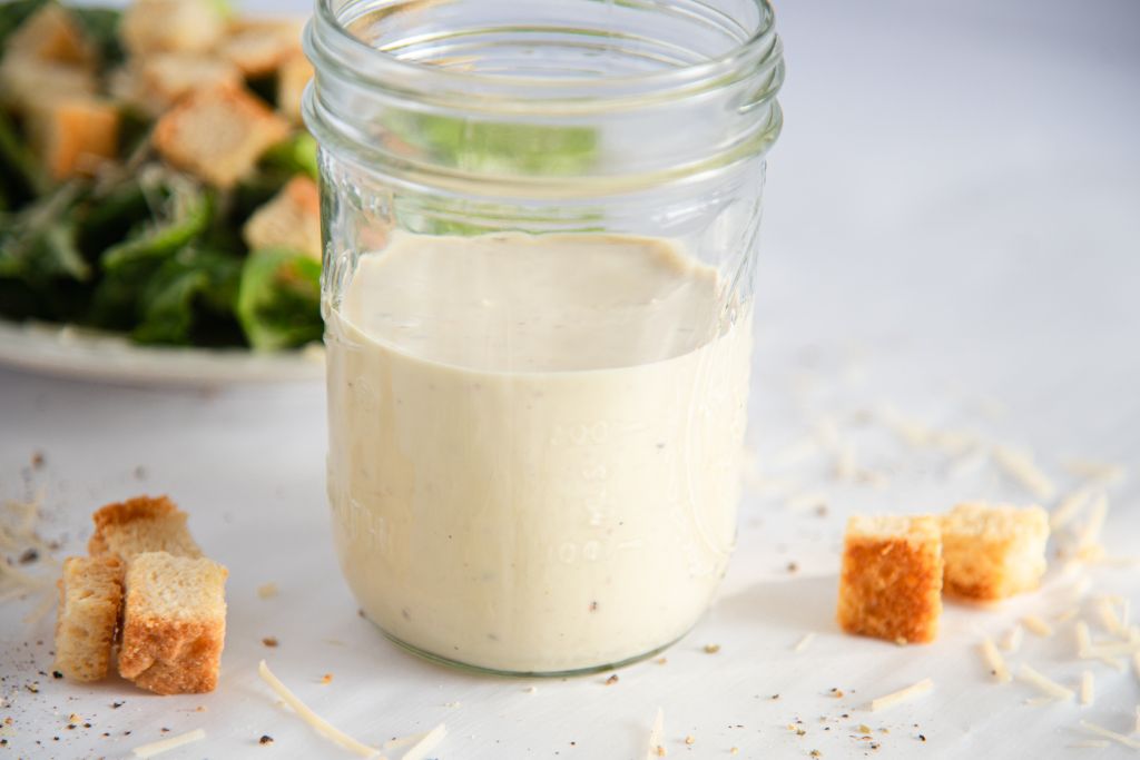 a close up of a jar of dressing with croutons and cheese sprinkled around it