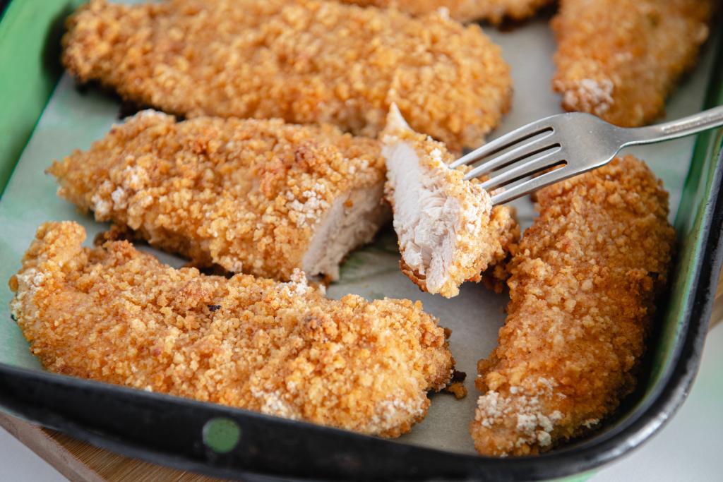 a cut piece of fried chicken with a fork in it, the fork is turned so you can see he chicken under the breading