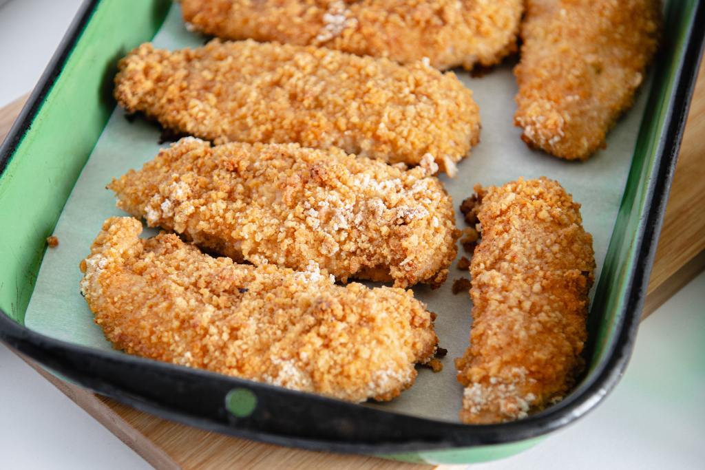 a green dish of fried chicken on a wooden cutting board