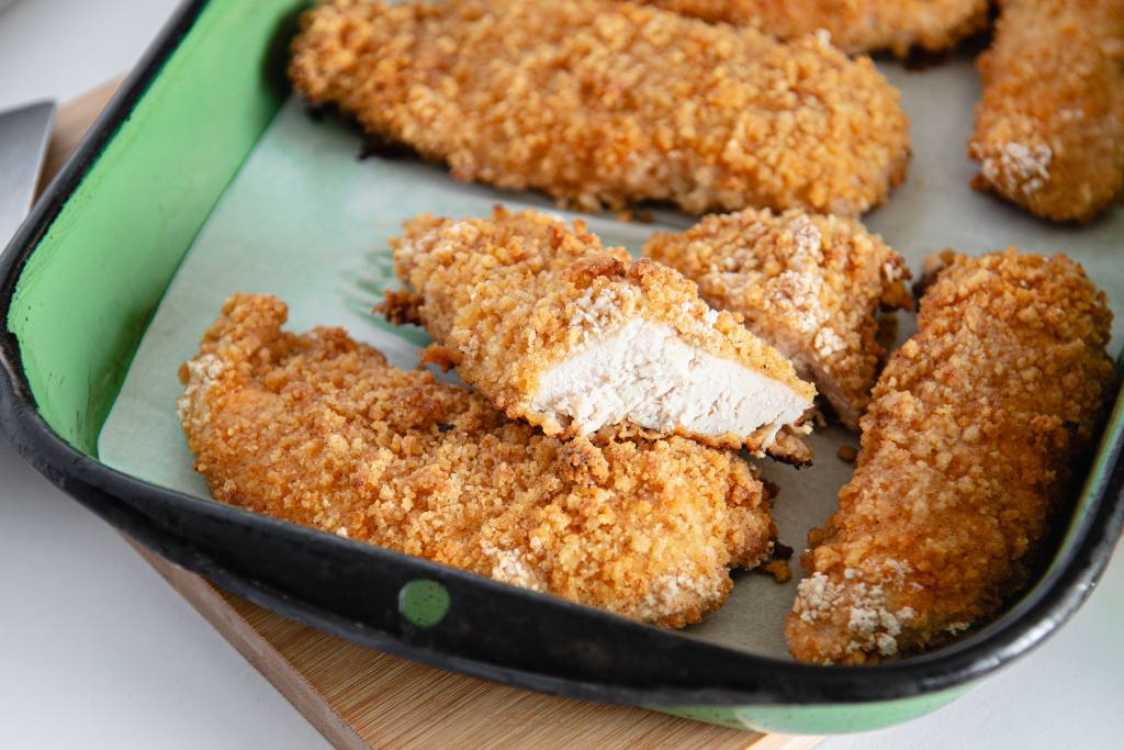 a green dish of fried chicken, set on a wooden cutting board, one of the pieces of chicken is propped on another piece of chicken