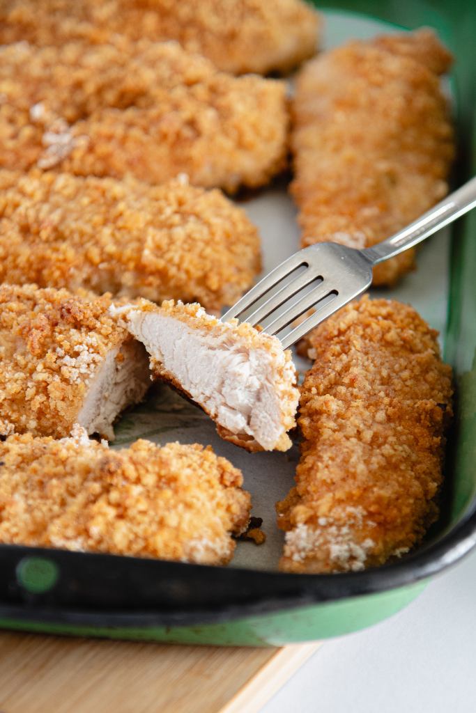 a piece of cut fried chicken with a fork in it, the chicken is turned so you can see the meat under the breading