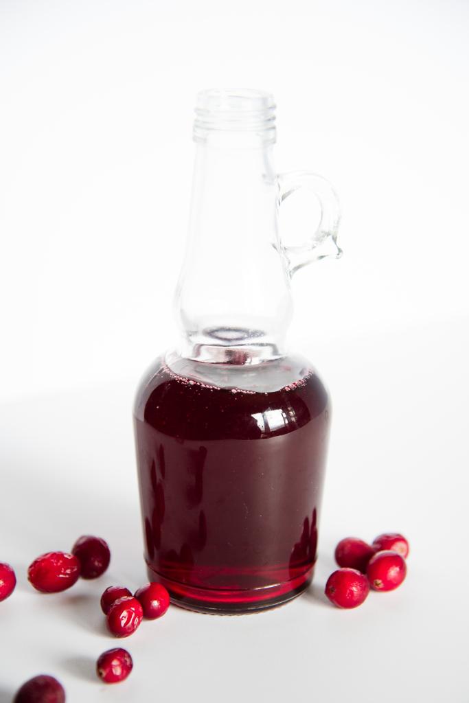 a bottle of cranberry simple syrup with fresh cranberries around it 