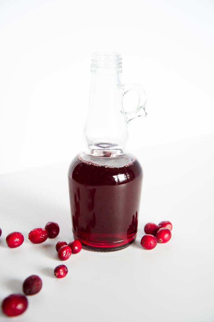 a bottle of cranberry syrup with fresh cranberries around it 
